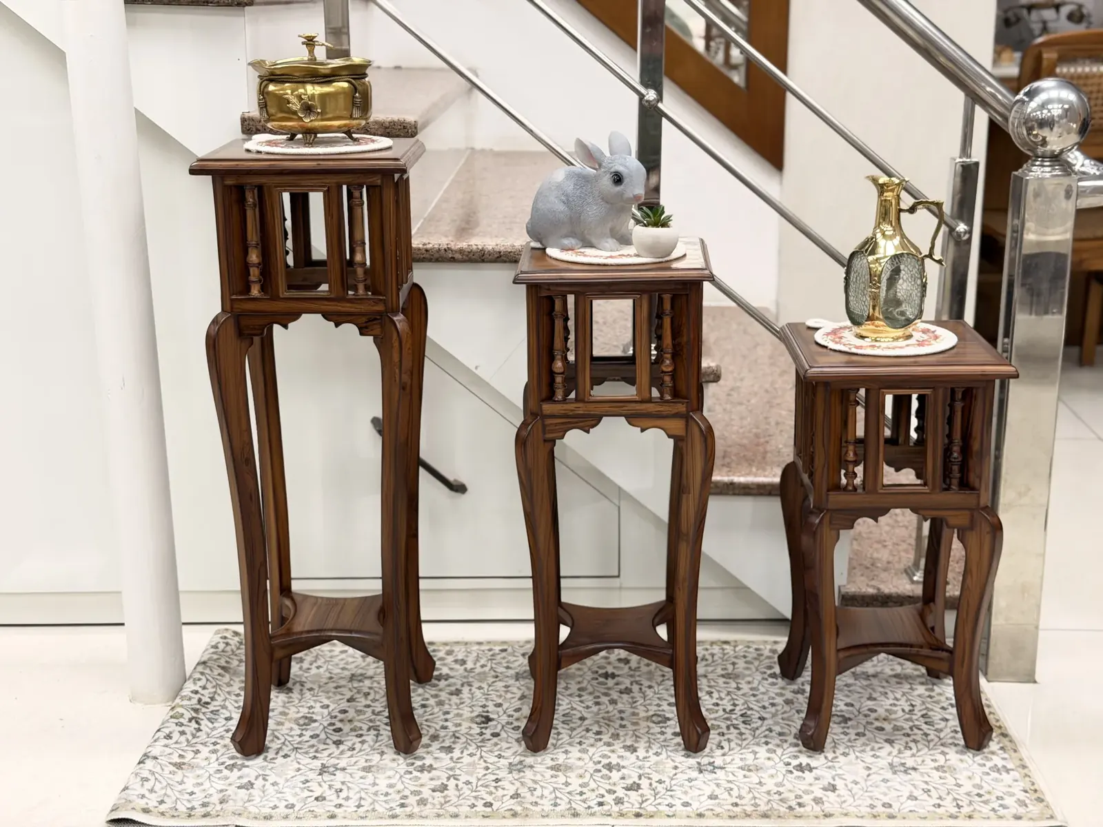 Graduated trio of solid teak cabriole display pedestals with brass heritage vases